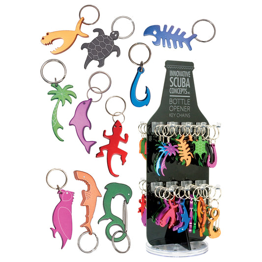 Collection of colorful bottle opener keychains in various marine-themed shapes including fish, sharks, dolphins, sea turtle, octopus, and palm tree, displayed alongside a retail display stand containing multiple keychains from Innovative Scuba Concepts